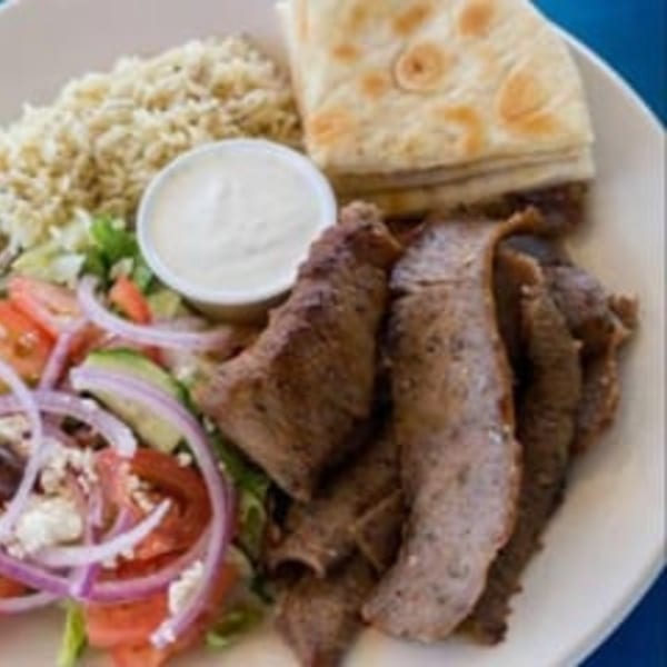 A gyro plate with sliced meat, rice, salad, pita bread, and a side of tzatziki sauce.