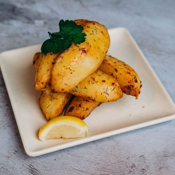 Golden roasted Greek potatoes with herbs and a lemon wedge on a white rectangular plate.
