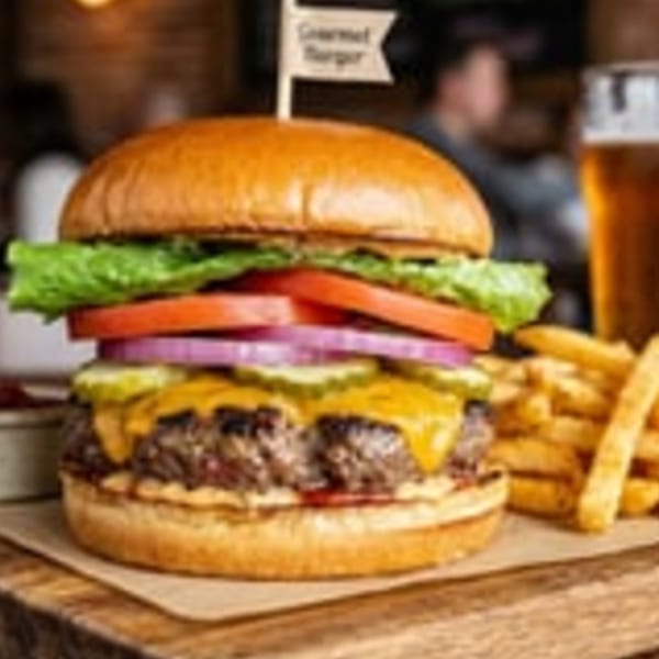 Gourmet burger with cheese, lettuce, tomato, onion, pickles, fries, and a beer.