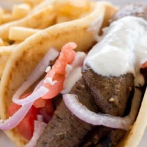 A close-up of a gyro with meat, tomatoes, red onions, and tzatziki sauce, served with fries.