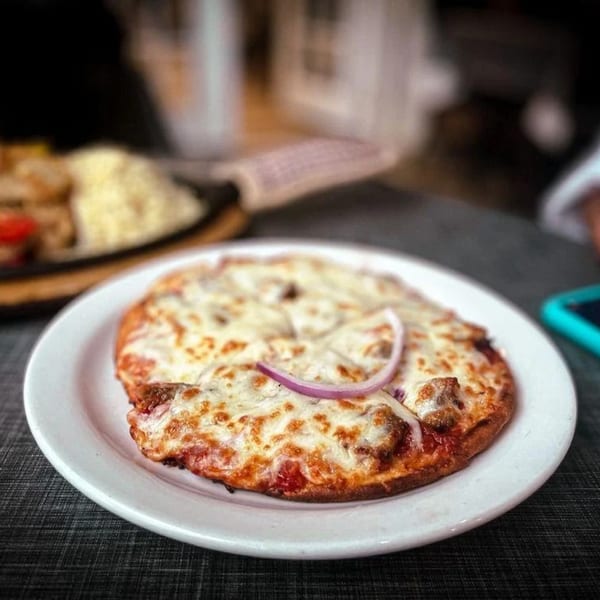 A small, cheesy Greek pizza with red onion slices on a white plate.